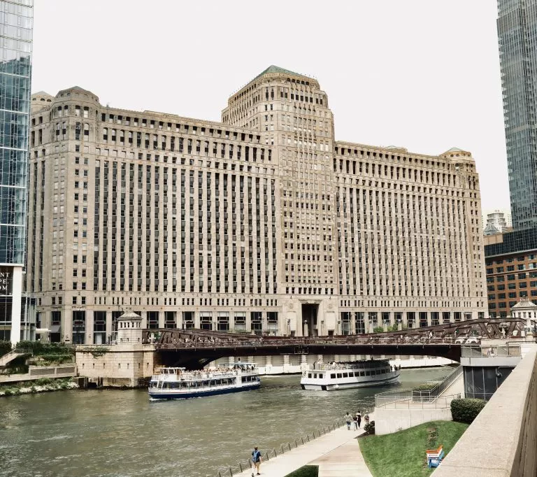 The Merchandise Mart in Chicago with two tourist site seeing boats sailing under a bridge